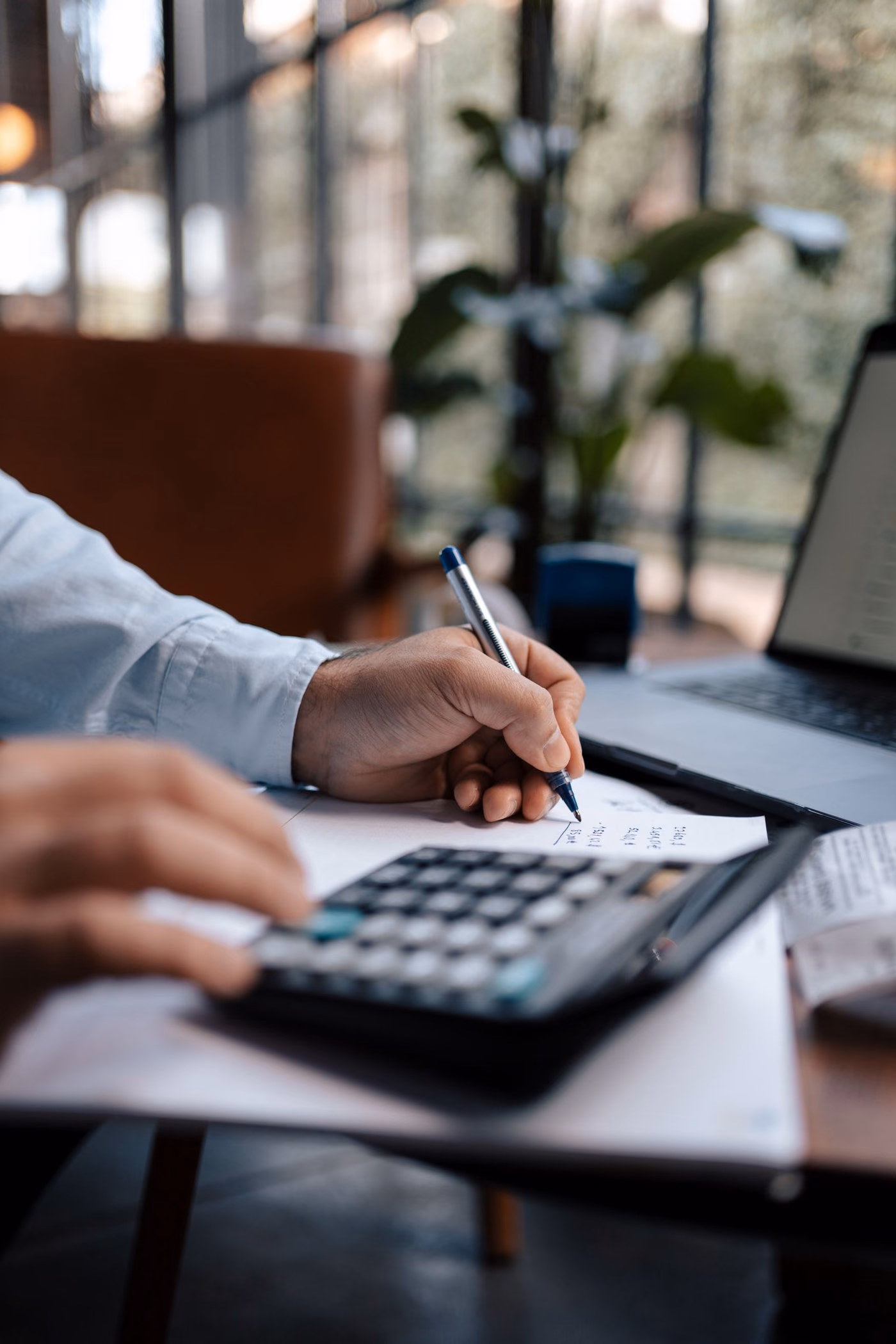 Mão fazendo cálculo de custo com calculadora e caderno de anotações